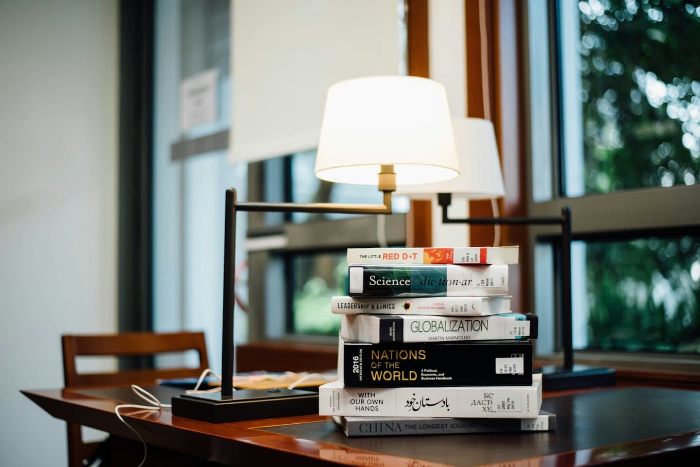 Libros académicos apilados sobre un escritorio de madera pulida.