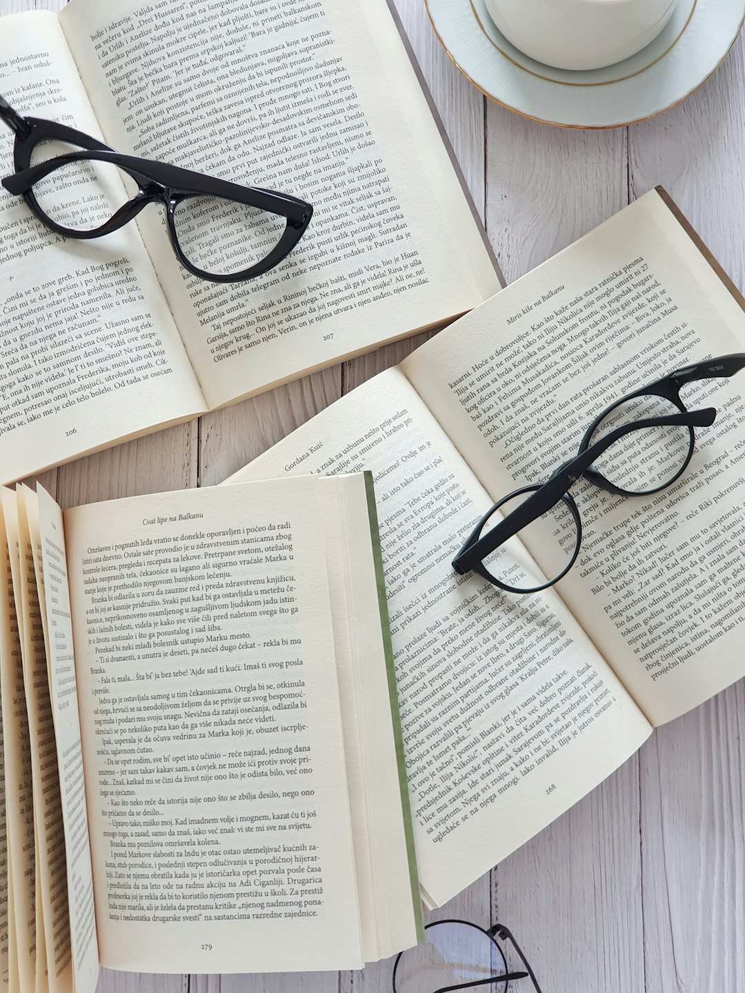 Libros abiertos y gafas de lectura junto a una taza de té sobre madera.